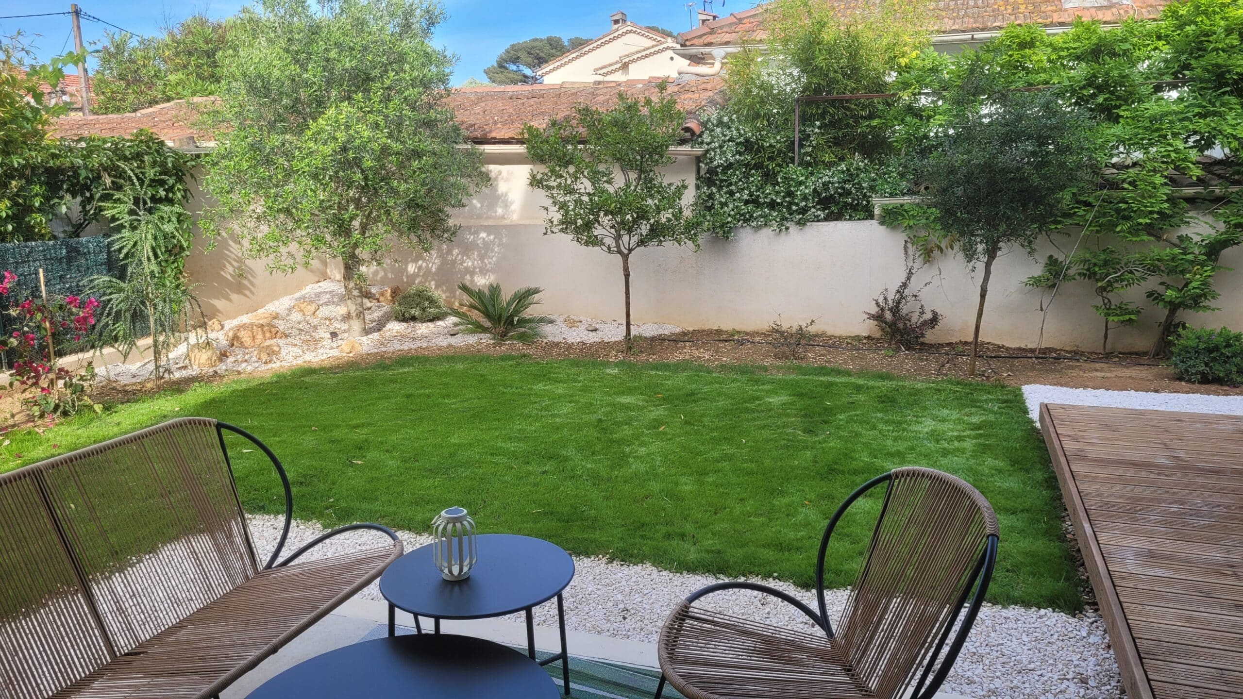 Terrasse avec mobilier design, pelouse verte et oliviers. Espace de détente élégant dans un jardin paysager.